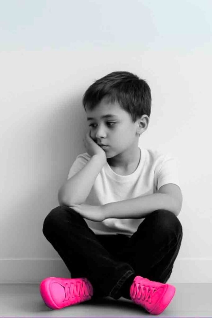 Niño sentado solo en el suelo, con gesto pensativo, sin juguetes ni pantallas. Fondo blanco, estética minimalista.